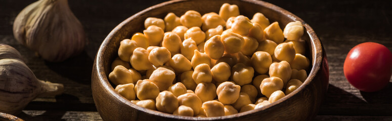 delicious chickpeas in bowl near garlic and cherry tomato on wooden rustic table, panoramic shot
