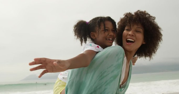 Smiling African American woman mother giving daughter a piggyback ride at the beach