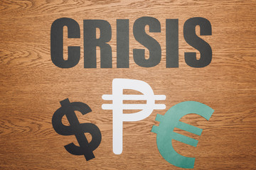 top view of dollar, peso and euro paper cut symbols, and word crisis on wooden desk