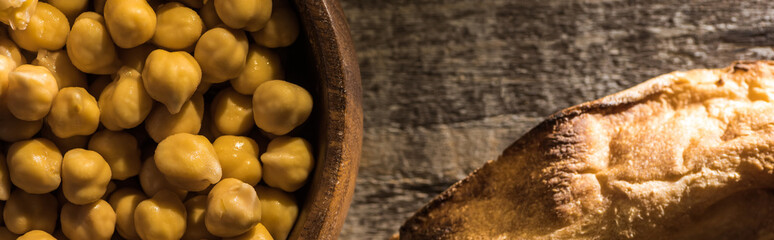 top view of chickpeas in bowl near fresh baked pita on wooden rustic table, panoramic shot