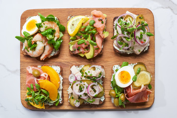 top view of wooden cutting board with tasty smorrebrod sandwiches on white marble surface
