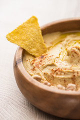 close up view of delicious hummus with nacho in bowl on beige wooden table