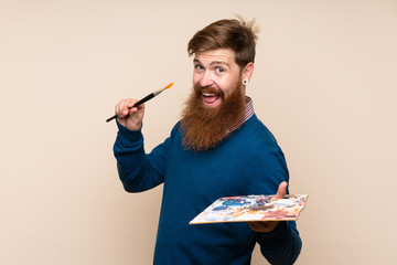 Redhead man with long beard over isolated background holding a palette