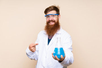 Redhead man with long beard over isolated background with a scientific test tube and pointing it