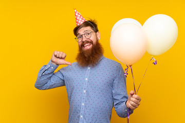 Redhead man with long beard holding balloons over isolated yellow background proud and...