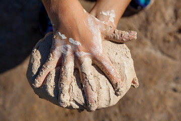 The child holds wet sand by hands