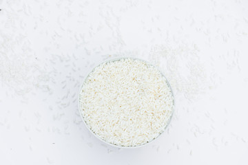 Milled rice in a cup and milled rice spread on a white ground