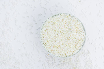 Milled rice in a cup and milled rice spread on a white ground