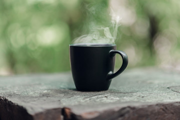 Black big cup of black tea with white steam on stone balcony edge in morning light with copy space.