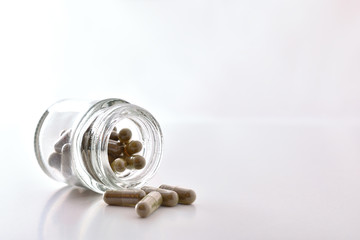 Glass jar filled with medication capsules on white table front