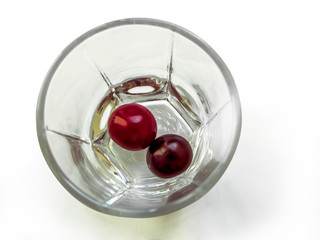 Two red berries of a cherry on the bottom of an empty glass cup, top view. Juicy ripe red fruits in a round transparent bowl