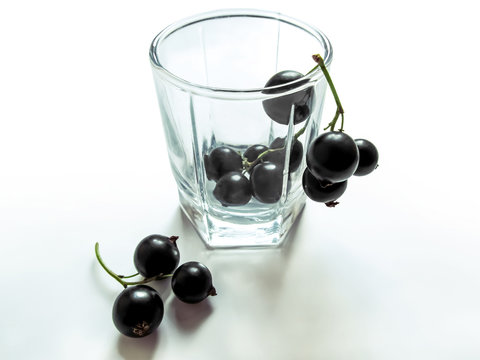 Bunches of blackcurrant in a glass cup close-up, isolated on a white background. Black berries with green stems near an empty transparent glass