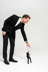 smiling businessman in suit playing with marionette with laptop on grey background