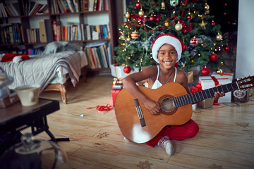 Fototapeta premium Girl in front of decoration Christmas tree play guitar.
