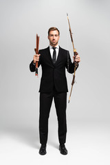 handsome businessman in suit holding bow and arrows on grey background