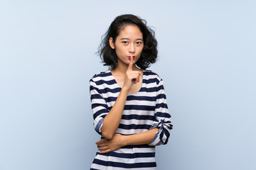 Asian young woman over isolated blue background showing a sign of silence gesture putting finger in...