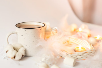 Hot cocoa with marshmallows and candles on a white background. New Year composition with white christmas tree decorations.