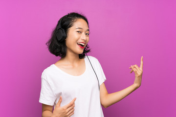 Asian young girl listening music with a mobile and dancing over isolated purple wall