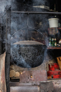 A stew or a soup is being prepared in a bowl above an open fire. Smoke coming up past the old and burned bowl.