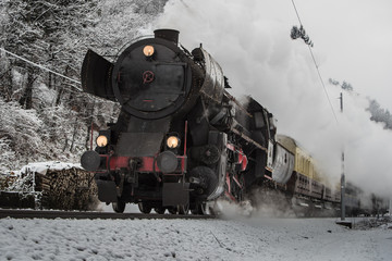 Christmas steam train on a gray winter day rushing towards camera and letting off steam - obrazy, fototapety, plakaty