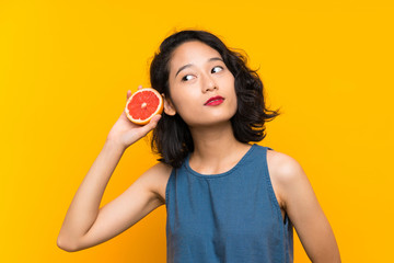 Young asian girl holding a grapefruit over isolated orange background