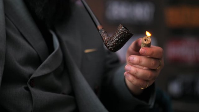 Close up of young business man with bearded holding smoking a tobacco pipe 