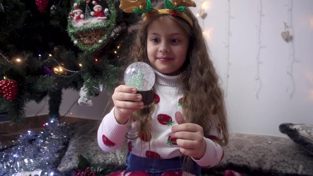 little girl shakes a snow globe and fools around. A child rejoices in a Christmas miracle.