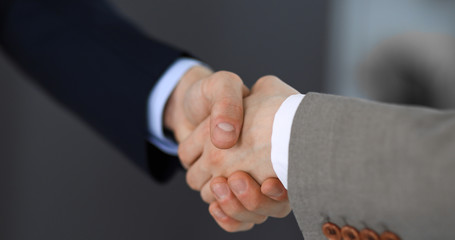Business people shaking hands while standing with colleagues after meeting or negotiation, close-up. Group of unknown businessmen and women in modern office. Teamwork, partnership and handshake