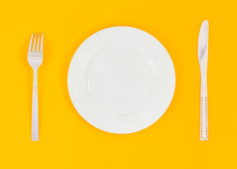 Empty plate, fork, knife on yellow background. Top view
