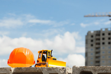 Builder's helmet and toy bulldozer in the construction site