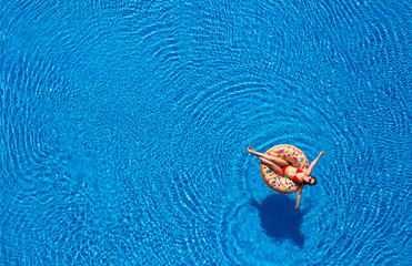 Aerial view of a woman in red bikini lying on a donut in the pool
