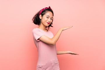 Asian young woman over isolated pink background holding copyspace to insert an ad