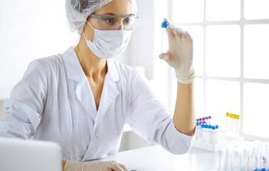 Professional female scientist in protective eyeglasses researching tube with reagents in laboratory. Concepts of medicine and research