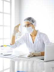 Professional female scientist in protective eyeglasses researching tube with reagents in laboratory. Concepts of medicine and research