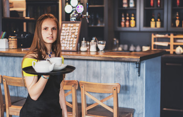 Portrait young waitress standing in cafe. girl the waiter holds in bunches a tray with utensils. Restaurant service