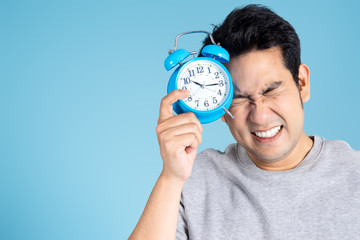Happy Asian man holding wake up clock on blue background and copy space.