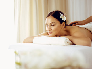 Obraz na płótnie Canvas Pretty brunette woman enjoying treatment with hot stones in spa salon. Beauty concept
