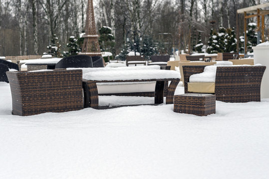 winter with heavy snowfall, wicker furniture: a table and two chairs covered with snow are on the street, there is a white, fluffy snow, an unusual, interesting picture of summer furniture for giving 