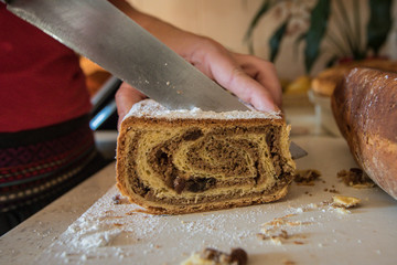 A person cutting a traditional slovenian dessert called potica with a knife on a kitchen desk.