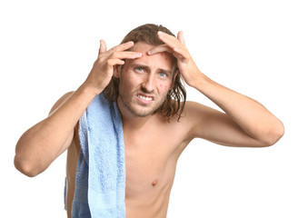 Portrait of young man with acne problem squishing pimples on white background