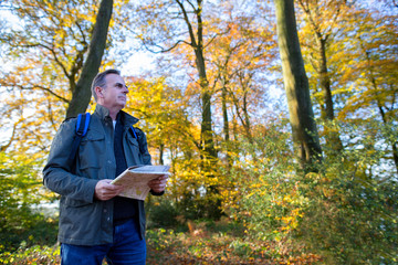 Fototapeta premium Active Mature Man With Map Walking Through Autumn Woodland In Slow Motion