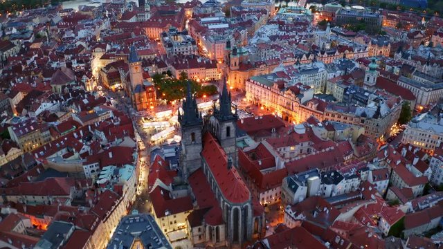 Aerial footage Church of Our Lady in old town district of Prague at twilight. Drone flying forwards to famous cathedral above night city with illuminated streets and red tiled roof buildings
