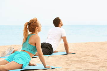 Sporty couple practicing yoga at sea resort