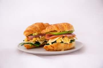 croissant sandwich of a ham, egg, spinach and avocado