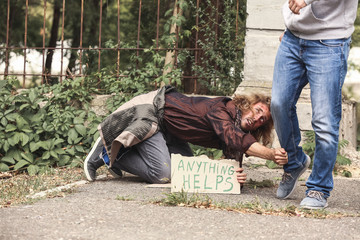 Poor homeless man begging passer-by for help outdoors