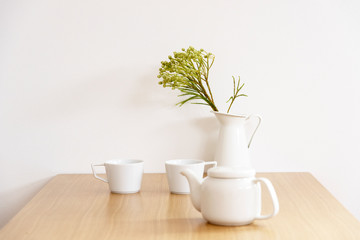 テーブルとお茶　ティーポット　マグカップ　白い食器　白い花瓶　観葉植物　カフェ　室内　部屋　屋内　白背景　白壁　ナチュラルな雰囲気　コピースペース　文字スペース　ホワイトスペース　余白　落ち着いた　リラックス　休憩