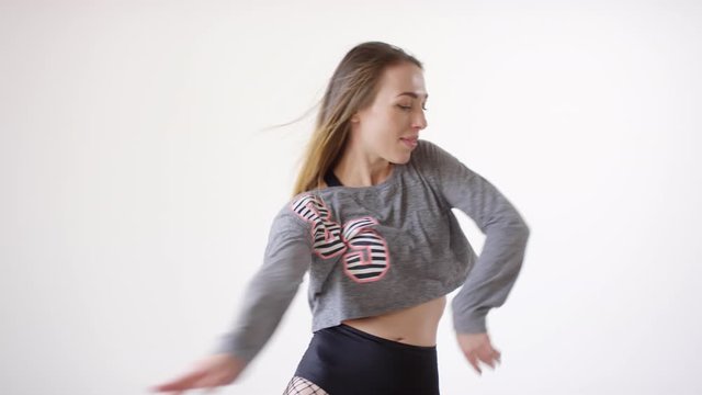 Tilt up shot of young seductive female dancer in fishnet tights, shorts and cropped sweatshirt dancing sensually in studio against white background