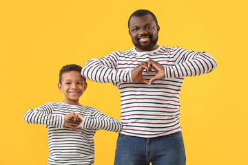 Portrait of African-American man and his little son making hearts with their hands on color...