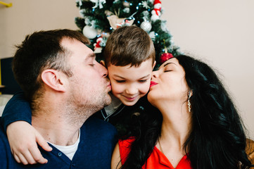Young family celebrating Christmas at home near the Christmas tree. Happy mom, dad and son enjoying their holiday time together.