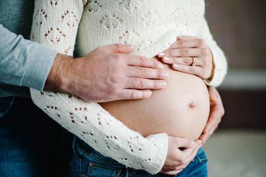 Cropped image of husband holding belly of his pregnant wife. Pregnant woman and loving handsome man hugging tummy at home. Loving Couple. Parenthood concept. Baby Shower.